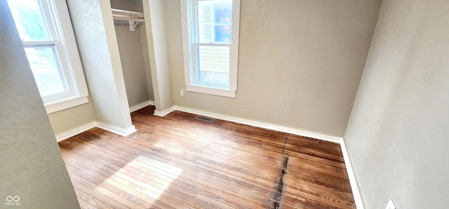 unfurnished bedroom with baseboards, visible vents, a textured wall, wood finished floors, and a closet