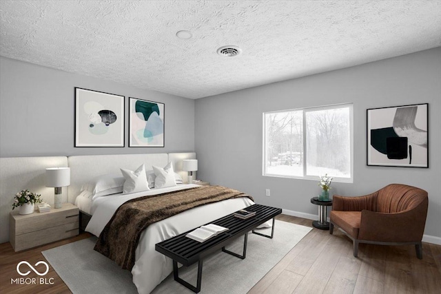 bedroom with visible vents, light wood-style flooring, baseboards, and a textured ceiling