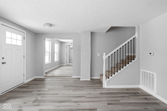 entryway featuring a textured ceiling, visible vents, baseboards, stairway, and light wood finished floors