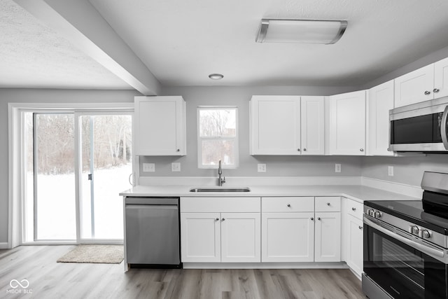 kitchen with stainless steel appliances, light countertops, a sink, and white cabinetry