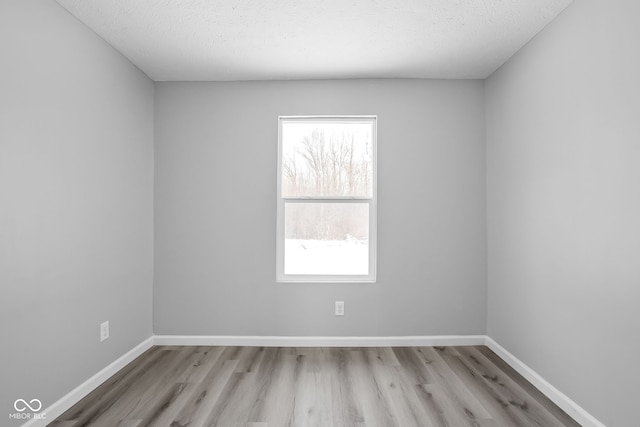 unfurnished room with a textured ceiling, light wood-type flooring, and baseboards