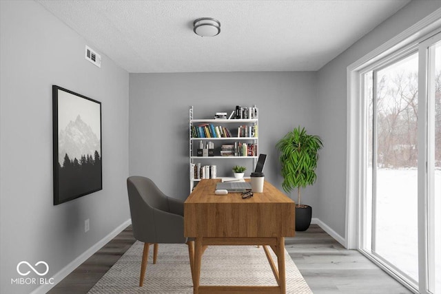 office featuring visible vents, baseboards, a textured ceiling, and light wood finished floors