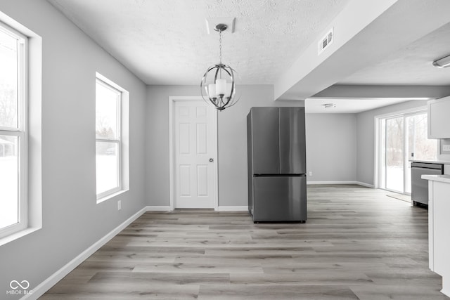 unfurnished dining area featuring a textured ceiling, light wood-style flooring, a notable chandelier, visible vents, and baseboards