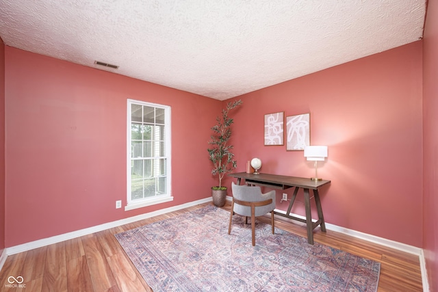 home office featuring baseboards, a textured ceiling, visible vents, and wood finished floors