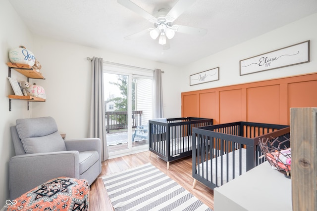 bedroom with a ceiling fan, light wood-type flooring, access to outside, and a decorative wall