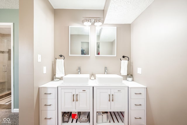 full bath with a sink, a shower stall, a textured ceiling, and double vanity