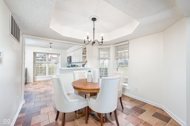 dining area with stone tile floors, a raised ceiling, visible vents, an inviting chandelier, and baseboards