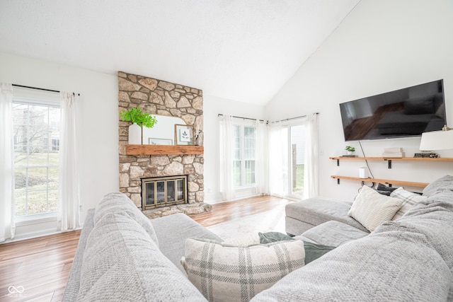 living area featuring high vaulted ceiling, a stone fireplace, a textured ceiling, and wood finished floors