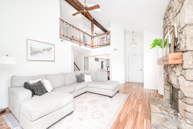 living room with high vaulted ceiling, ceiling fan with notable chandelier, a fireplace, wood finished floors, and beamed ceiling