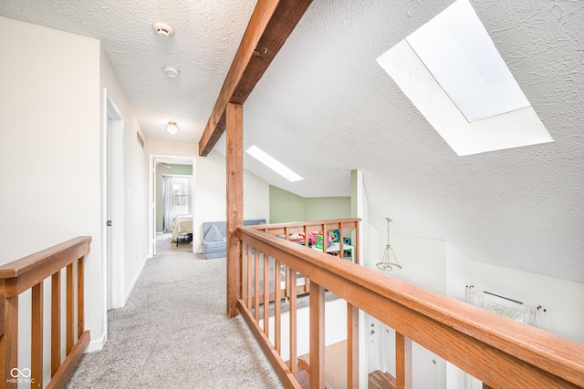 hallway featuring vaulted ceiling with skylight, a textured ceiling, carpet flooring, and an upstairs landing