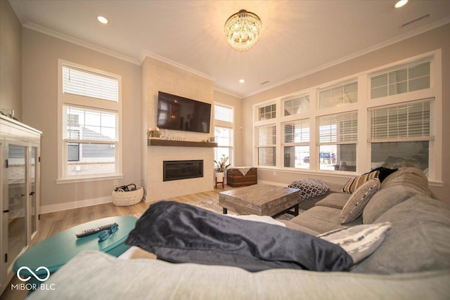 living area with crown molding, a tiled fireplace, wood finished floors, and a healthy amount of sunlight