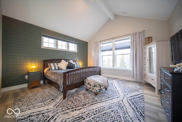 bedroom featuring vaulted ceiling with beams, an accent wall, multiple windows, and wood finished floors