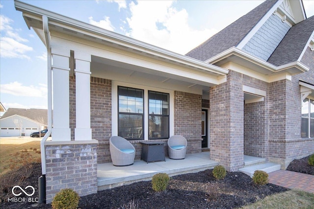 entrance to property with covered porch, brick siding, and roof with shingles