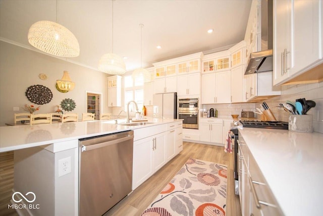 kitchen with light wood finished floors, decorative backsplash, light countertops, stainless steel appliances, and wall chimney range hood