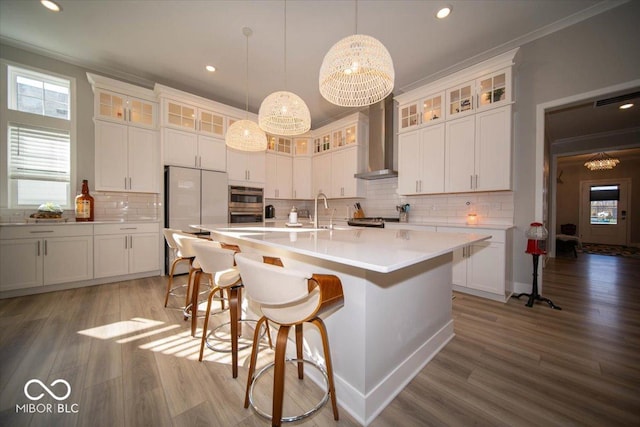 kitchen featuring wall chimney exhaust hood, ornamental molding, wood finished floors, and a center island with sink