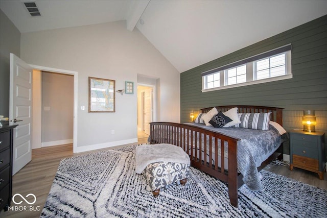 bedroom featuring high vaulted ceiling, wood finished floors, visible vents, baseboards, and beamed ceiling