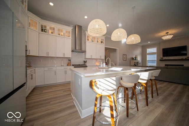 kitchen with light wood-style flooring, wall chimney exhaust hood, open floor plan, light countertops, and backsplash