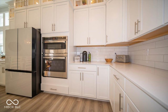 kitchen with white cabinets, stainless steel appliances, light countertops, light wood-style floors, and backsplash