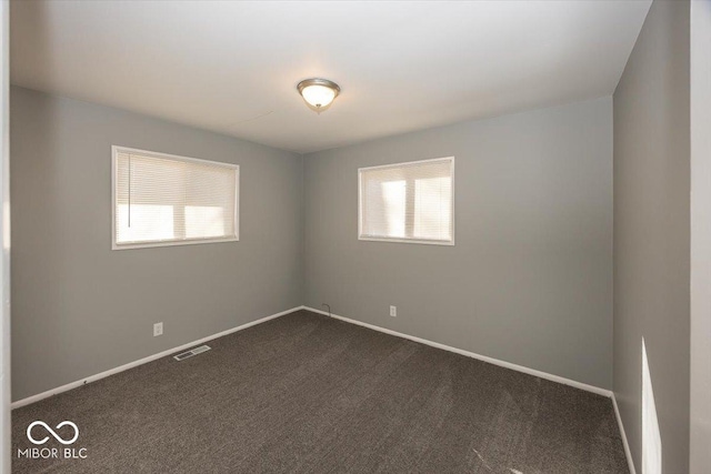 spare room with baseboards, visible vents, and dark carpet