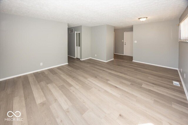 unfurnished room featuring visible vents, baseboards, a textured ceiling, and wood finished floors