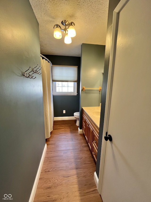 bathroom with toilet, a textured ceiling, vanity, wood finished floors, and baseboards