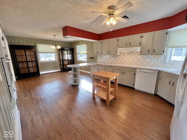 kitchen with dishwasher, wood finished floors, decorative light fixtures, light countertops, and under cabinet range hood