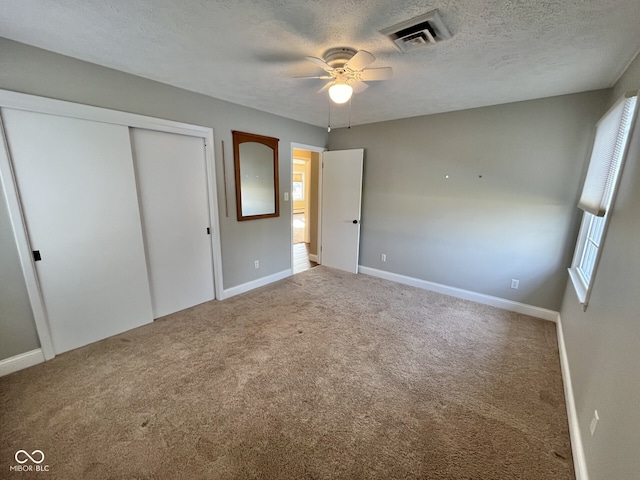 unfurnished bedroom featuring baseboards, visible vents, a textured ceiling, carpet flooring, and a closet