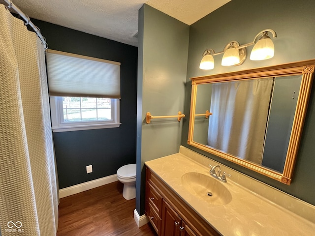 bathroom featuring toilet, a textured ceiling, vanity, wood finished floors, and baseboards