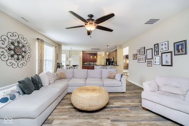 living room with ceiling fan, wood finished floors, visible vents, and baseboards