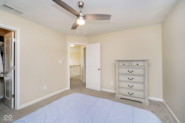 bedroom featuring baseboards, a walk in closet, visible vents, and light colored carpet