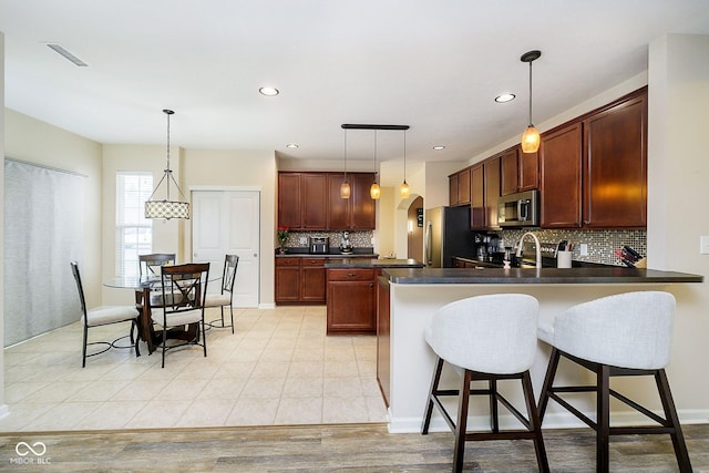 kitchen with arched walkways, stainless steel appliances, a peninsula, visible vents, and dark countertops