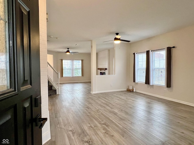 unfurnished living room with stairs, baseboards, wood finished floors, and a ceiling fan