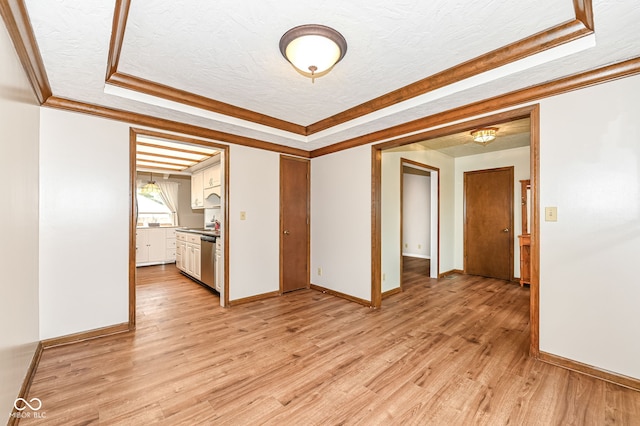 spare room with a textured ceiling, a tray ceiling, and light wood finished floors