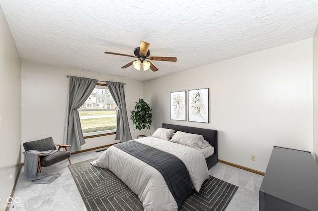 bedroom featuring light carpet, ceiling fan, a textured ceiling, and baseboards