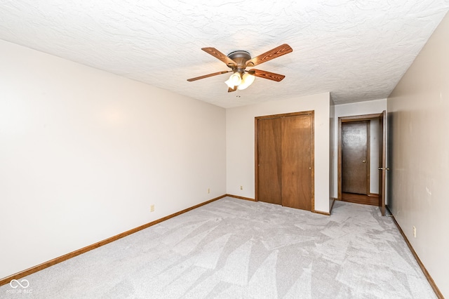 unfurnished bedroom with light carpet, a closet, a textured ceiling, and baseboards