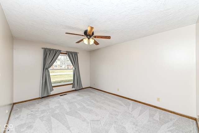 unfurnished room with light carpet, ceiling fan, a textured ceiling, and baseboards