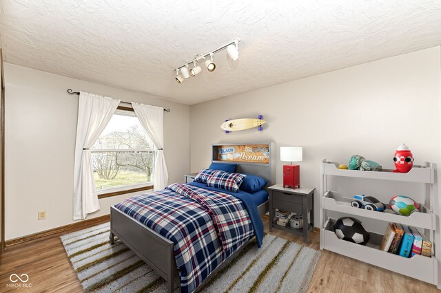 bedroom featuring rail lighting, a textured ceiling, baseboards, and wood finished floors