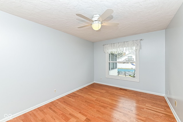 empty room with baseboards, visible vents, a textured ceiling, and light wood finished floors