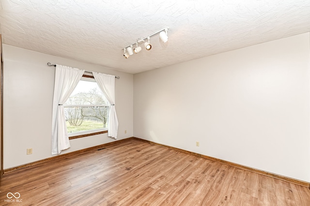 unfurnished room with light wood-type flooring, rail lighting, a textured ceiling, and baseboards