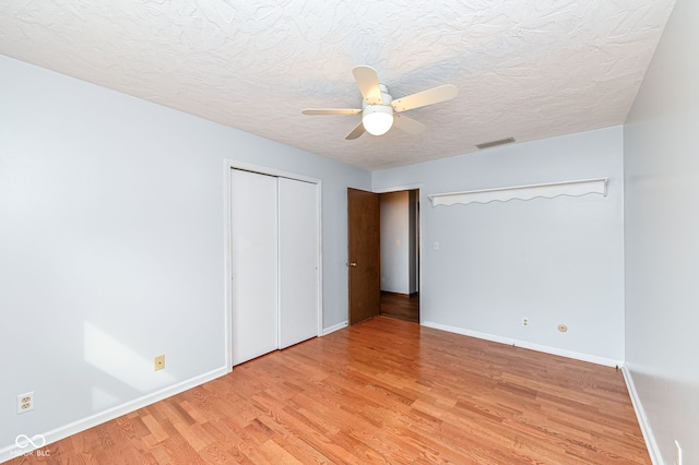 unfurnished bedroom featuring a closet, visible vents, light wood-style floors, a textured ceiling, and baseboards