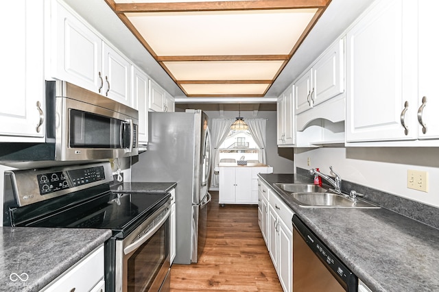 kitchen featuring light wood finished floors, white cabinets, dark countertops, appliances with stainless steel finishes, and a sink