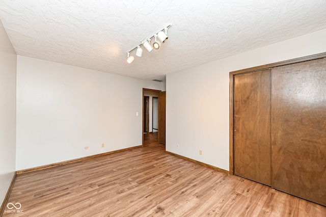 unfurnished bedroom with light wood finished floors, a closet, a textured ceiling, track lighting, and baseboards