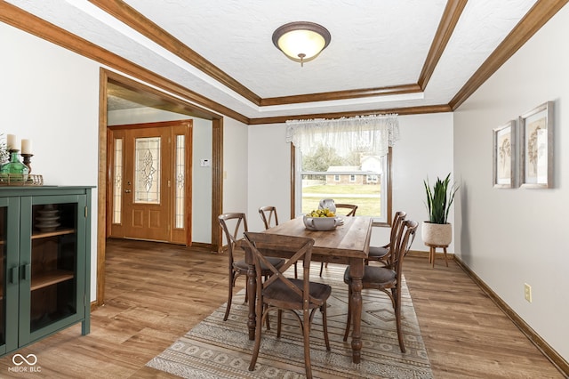 dining area with ornamental molding, a tray ceiling, a textured ceiling, and light wood-type flooring