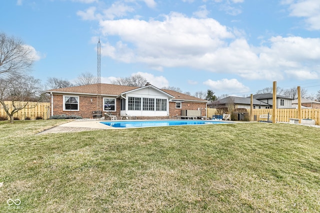 rear view of property featuring fence private yard, a fenced in pool, a lawn, and brick siding