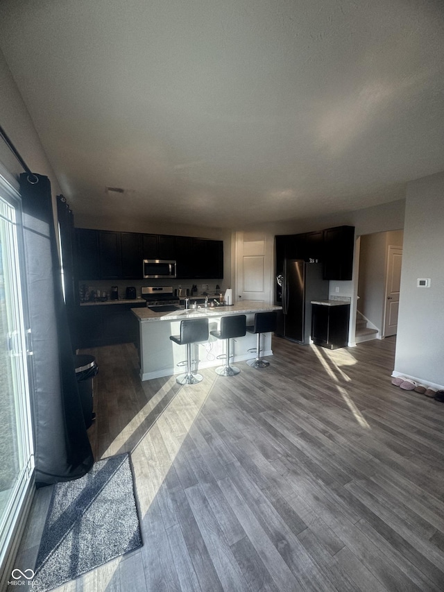 kitchen featuring stainless steel appliances, light countertops, an island with sink, and dark wood-style floors