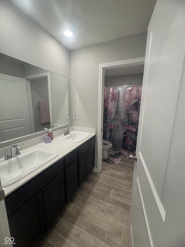 bathroom featuring double vanity, a sink, toilet, and wood finished floors