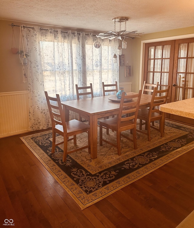 dining room featuring a wainscoted wall, a textured ceiling, hardwood / wood-style floors, and french doors