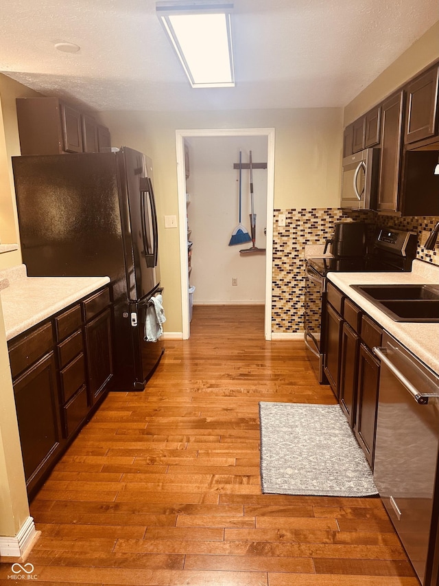 kitchen featuring light wood-style flooring, dark brown cabinetry, a sink, light countertops, and black appliances