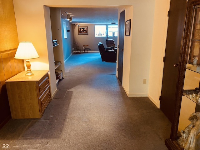 hall featuring dark carpet and baseboards