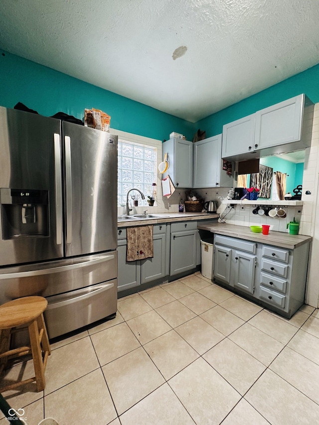 kitchen with stainless steel refrigerator with ice dispenser, light tile patterned floors, gray cabinetry, a sink, and a textured ceiling